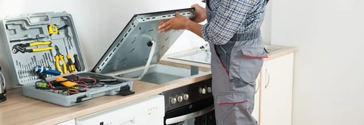 Cooktop repair technician lifting a built-in stovetop for service in Long Beach, CA
