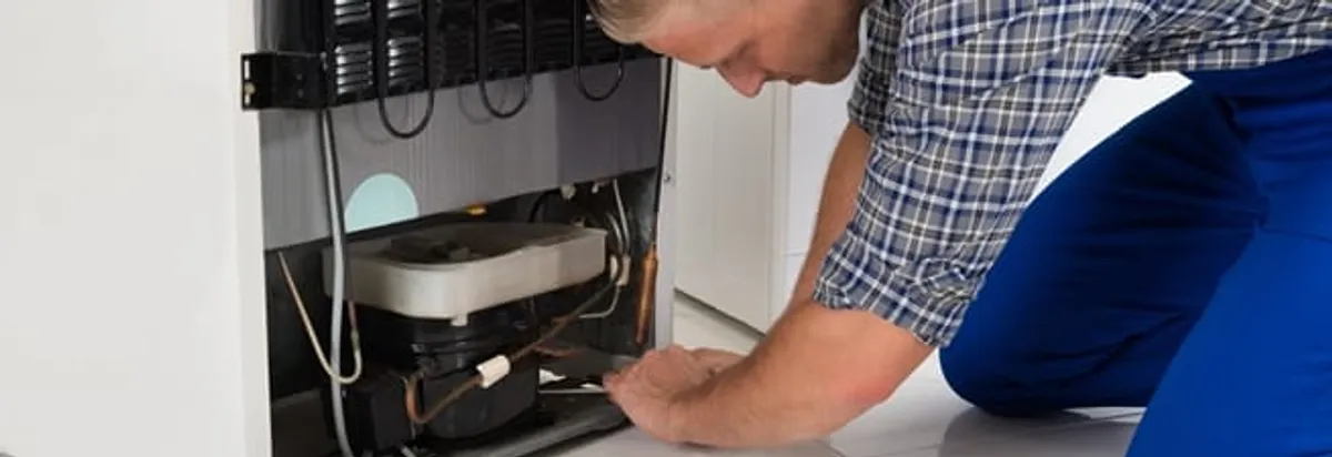 Refrigerator repair technician servicing the compressor and condenser area in Long Beach, CA