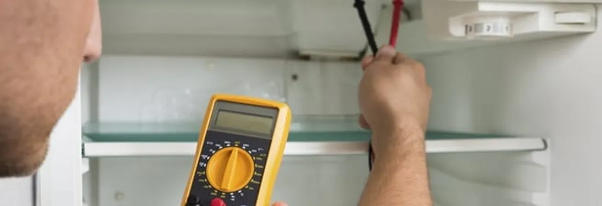 Refrigerator repair technician testing electrical components with a multimeter in Long Beach, CA