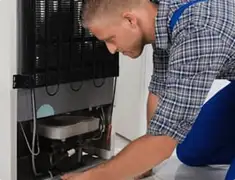 Refrigerator repair technician servicing the compressor and condenser area in Long Beach, CA